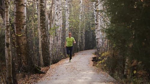 Fit Man Sprinting Along a Winding Birchtree Trail at Sunrise Focused on Training and Enjoying an