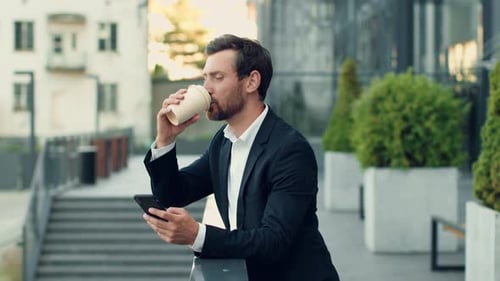 Man Using Phone And Drinking Coffee Outdoors