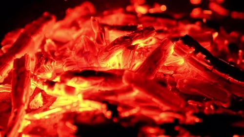 Sparkling pieces of embers in the pile. Close view of the burnt out wood smoldering at dark backdrop