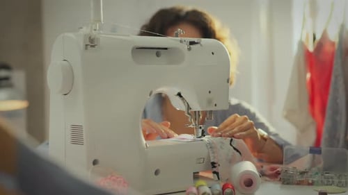 Tailoring. In a weaving shop, a pretty Asian girl works intently on a sewing machine. A dynamic