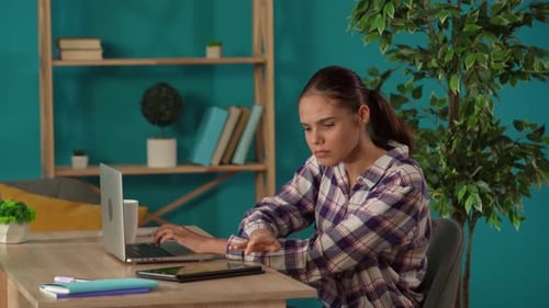 Medium Shot Capturing a Woman Working on a Laptop and Checking His Tablet in Her Home Office Young