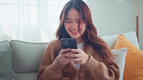 Smiling Woman Using Smartphone on Couch at Home