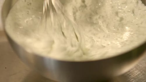 Whisking ingredients in a metal bowl to create a creamy mixture, panning close-up