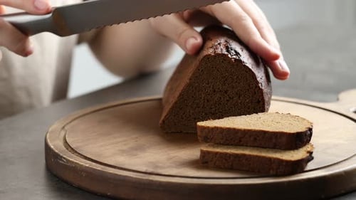 Woman cutting fresh rye bread at table, closeup