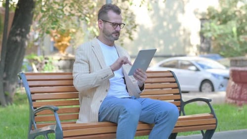 Man Sits on Bench Using Tablet in Park