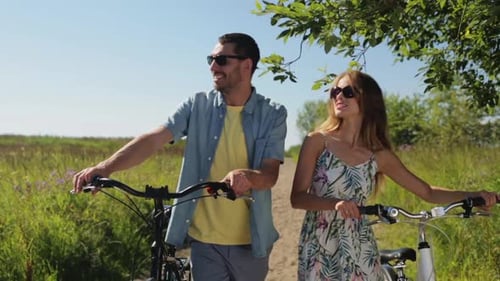 People And Lifestyle Concept - Happy Young Couple With Bicycles Walking And Talking Along Road At...