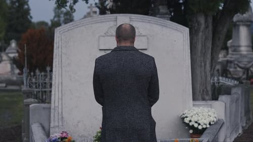 A Man Standing Solemnly in a Cemetery Before a Gravestone During the Peaceful Twilight Hours