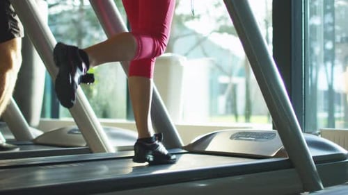 Nahaufnahme von männlichen und weiblichen Beinen, die im Fitnessstudio auf dem Laufband laufen.