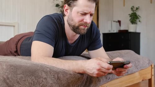 Man Uses Smartphone Lying on Bed at Home