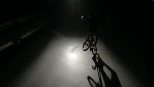 Young bmx rider performing extreme tricks in a dark urban warehouse