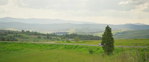 Beautiful Landscape White Car on a Rural Mountain Road Surrounded By Green Hills Forest Summer Time