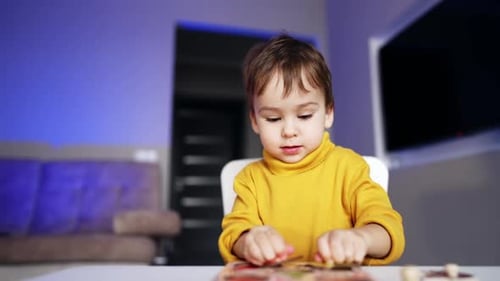Adorable toddler boy in yellow sweater holds two pieces of puzzles.