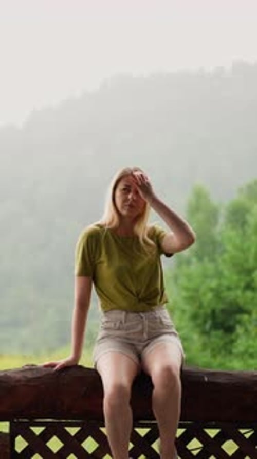 Attractive Lady Touches Hair Sitting on Log Against Mountain