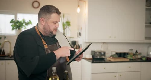 Man Reads Tablet Recipe in a White Kitchen