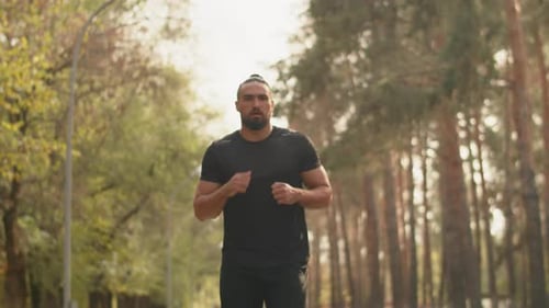 Young Muscular Sportsman Running in the Alley of a City Park at a Steady Pace on a Sunny Day Concept