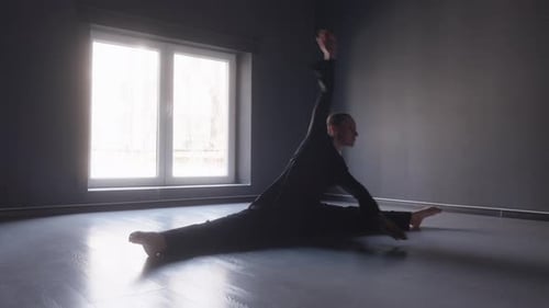Flexible Dancer Performs Front Split in a Dark Studio with a Large Window