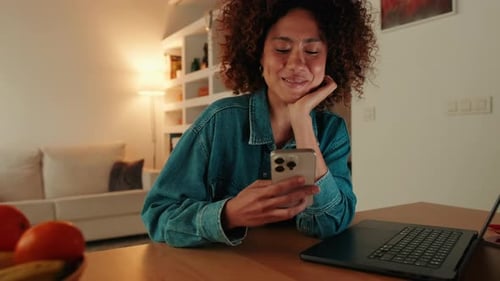 Smiling woman sitting at table in living room having fun with mobile phone