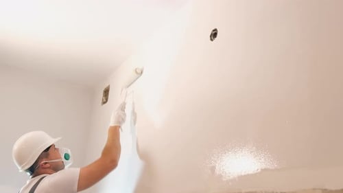 Side View of a Craftsman Painting a Wall with a White Paint Roller Painting the Walls in the House
