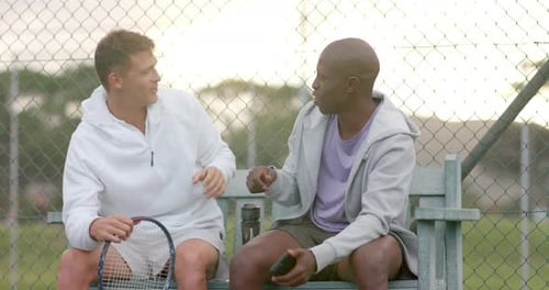 Happy diverse male friends looking at smartphone and shaking hands at tennis court, slow motion