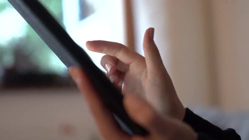 Close side view shot of a woman's hands using a tablet, scrolling on touch screen.