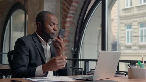 Man Works at Laptop, Talks on Phone in Office