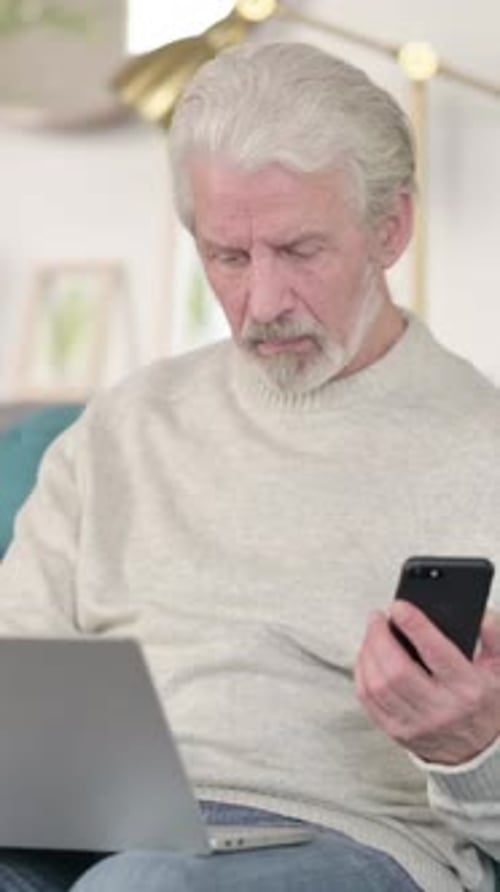 Senior Man Using Phone with Laptop on Lap