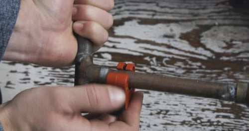 Una conexión de tubería de cobre vieja se abre con manos masculinas con un cortatubos. Ángulo alto, toma estática.