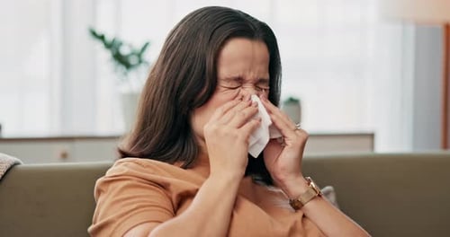 Woman with Tissue Sits on Couch Indoors