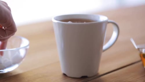 Unhealthy Eating and Drinks Concept - Hand Adding Sugar to Cup Of
