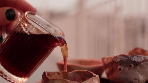 Close Up Side View Pouring Tea From Transparent Milk Jug Into Cup