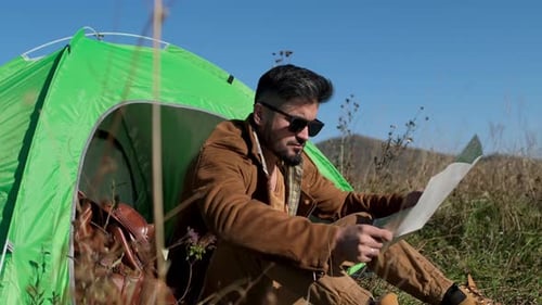 Man Looking at Map Outside Green Tent