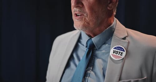 Man in Suit Speaking with "Vote" Button