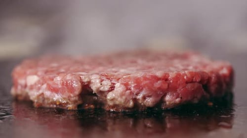 A high quality shot of a delicious pink juicy sizzling beef patty being grilled or fried on a