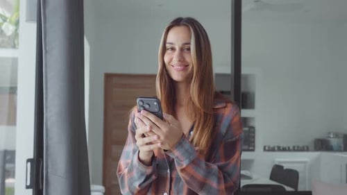 Happy User Smiling Woman Holding Smartphone Looking at Camera in Modern Home Happy User Enjoying