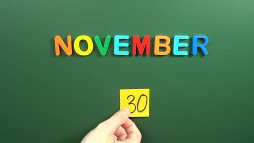 Hand sticking a sticker 30 November calendar day on school board. 30 date of November. Thirtieth