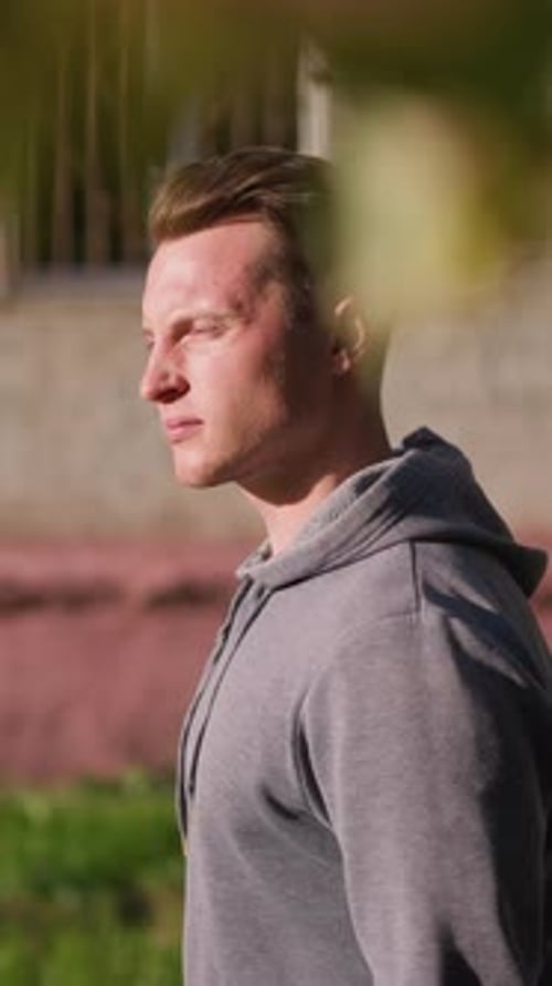 Young Man in Gray Hoodie Looking Thoughtfully Into Distance By Aged Building