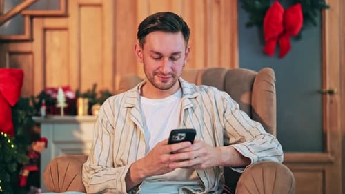 Man Using Phone Sitting in Chair at Christmas