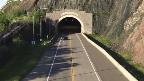 Aerial, black luxury supercar driving out of tunnel during the day