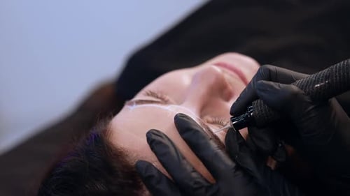 Beautician uses a special device to apply permanent make up on client’s eyebrows.
