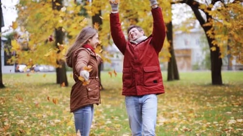 Happy young couple throws autumn leaves up in the park on beautiful fall day