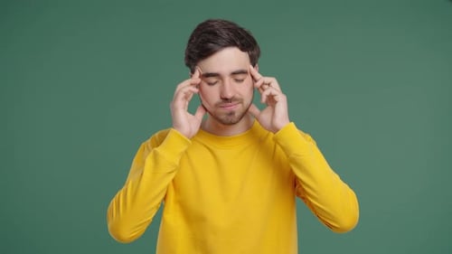 Stressed Man Massaging Temples Against Green Background