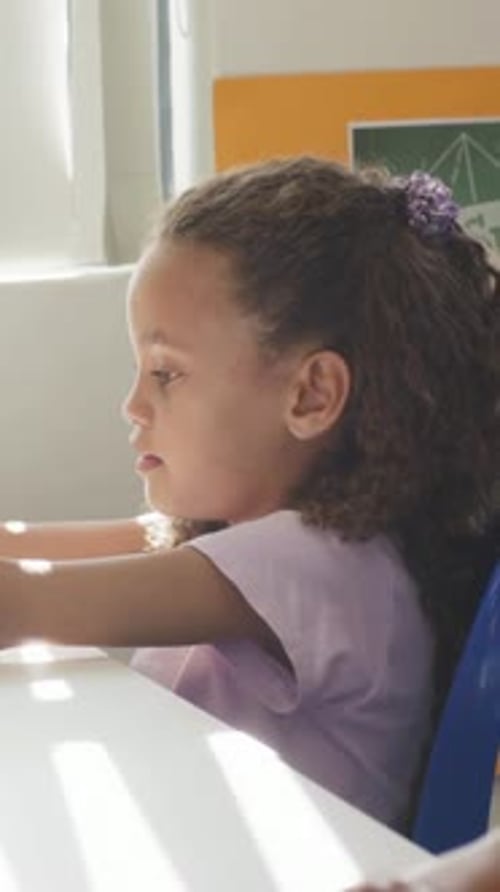 Vertical video: Responding to off-frame cue, student in purple shirt raising hand at table, blinds
