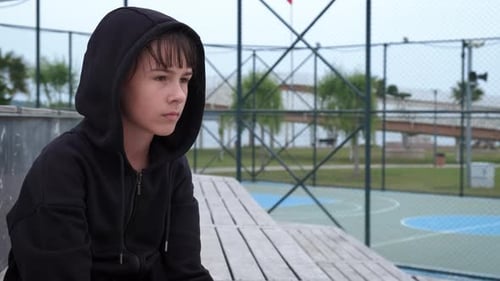 Loneliness. A sad, lonely teenage girl sits alone on the sports ground.