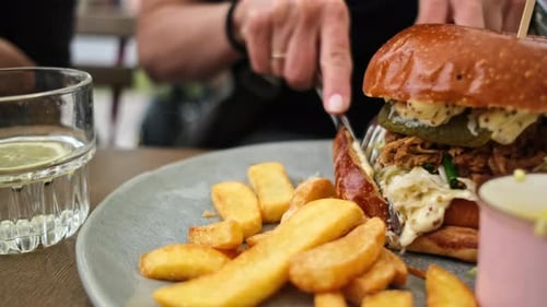 Chica cortando una jugosa hamburguesa de carne grande en un café de comida rápida al aire libre