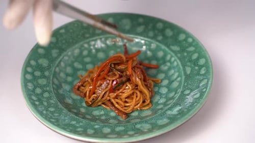 A chef lays out spaghetti on a plate in a restaurant
