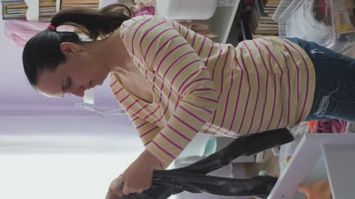 Woman Folding Baby Clothes in Children's Room