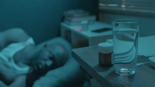 Man Asleep at Night Beside Water and Pills