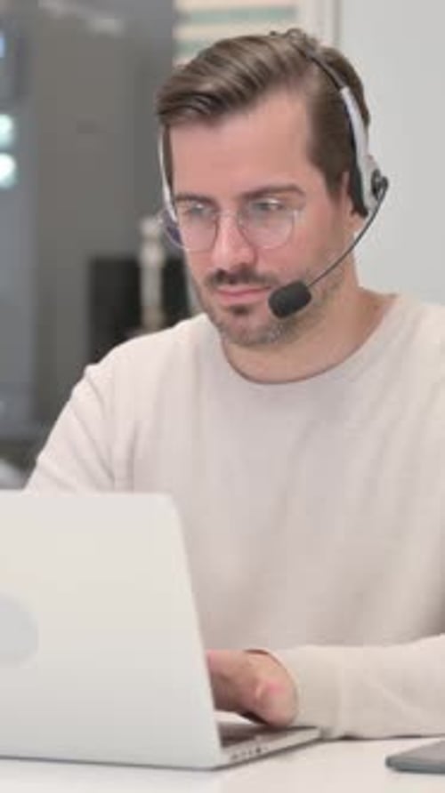 Young Man with Headset Working on Laptop in Call Center