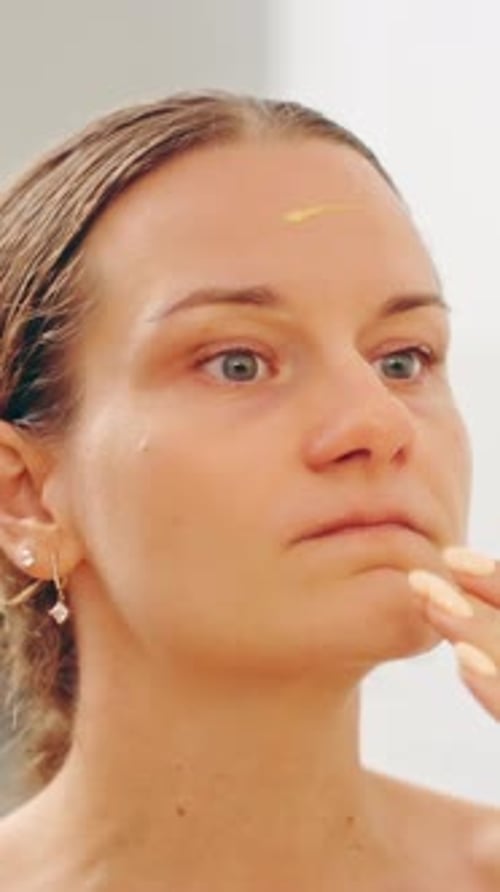 Vertical video. Woman Using Fingertip to Gently Spread Retinol Serum on Chin Area While Looking in M