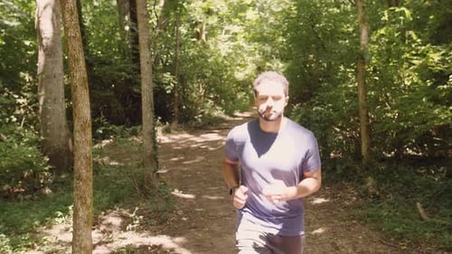 Young mixed male running through forest trail in shadow